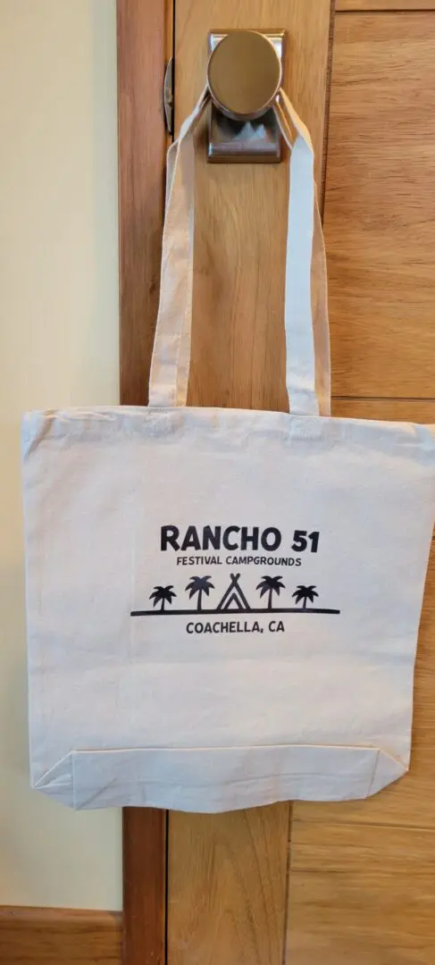 A white hand bag written rancho 5i in black hung on a door